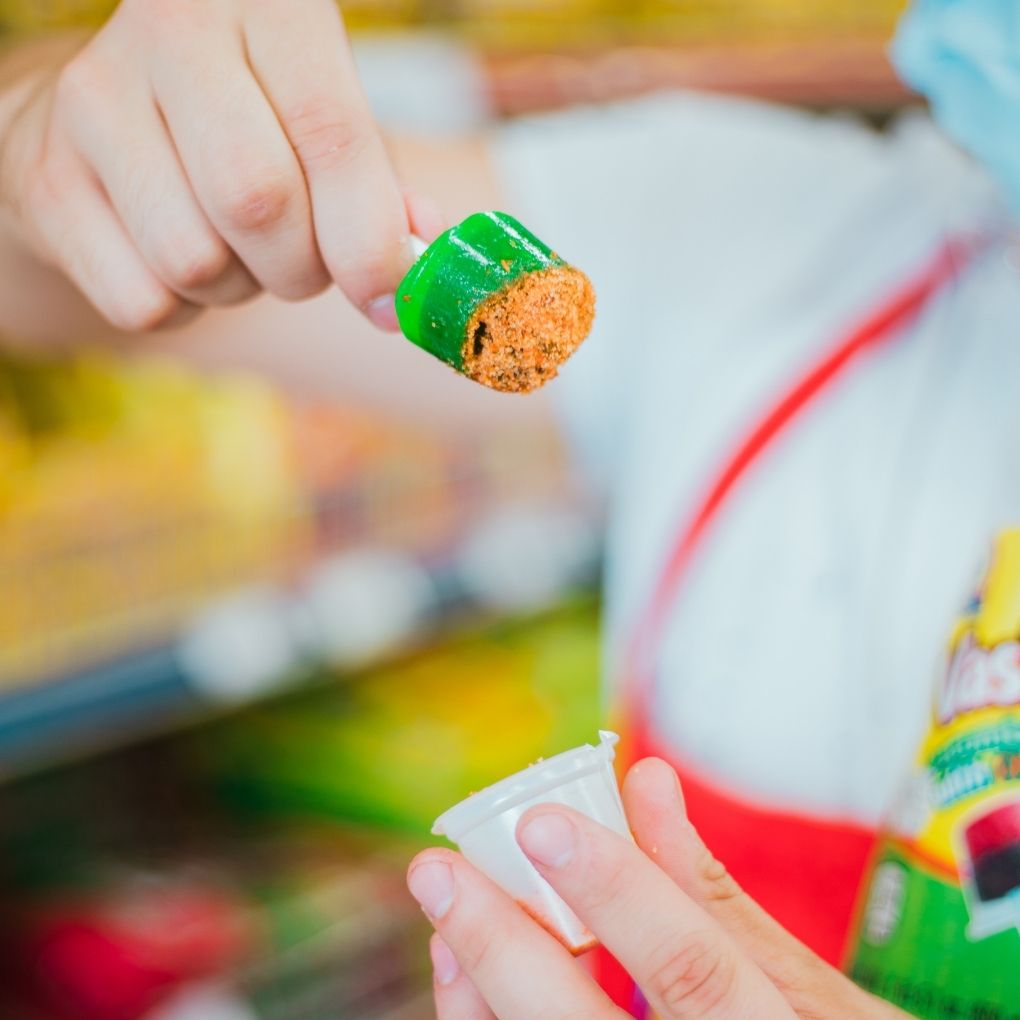 Green cucumber hard candy lollipop dipped in chili powder Mexican candy